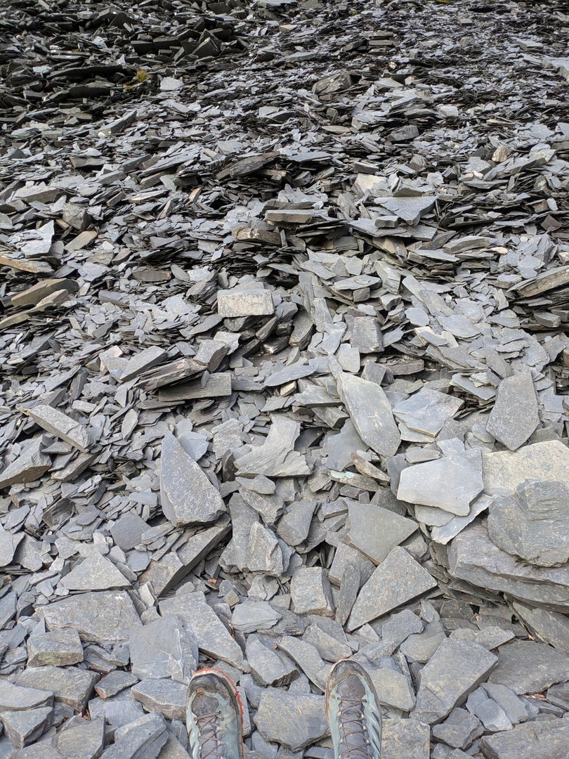 A huge pile of broken slate, filling the whole picture, with a pair of booted feet at the bottom.