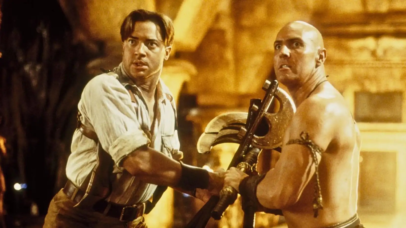 Image from Universal Studios The Mummy Returns (2001). It shows Rick, a muscular man with short brown hair, tussling with axes against his enemy, the bald Imhotep.