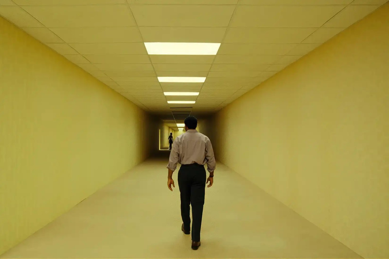 Clark (Chiwetel Ejiofor) walks through a long hallway with yellow walls, floor, and ceiling panels in Backrooms