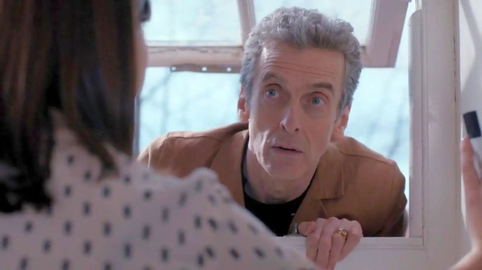The Twelth Doctor peers through a window.
