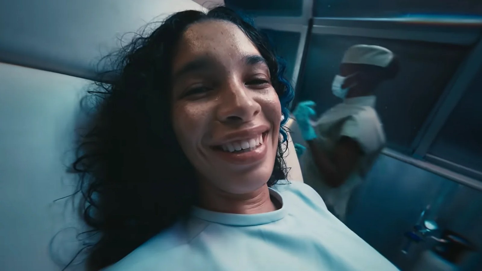 Screenshot from Humankind 2's announcement trailer, showing a woman in a hospital gown smiling into the camera while laying on an operating table.