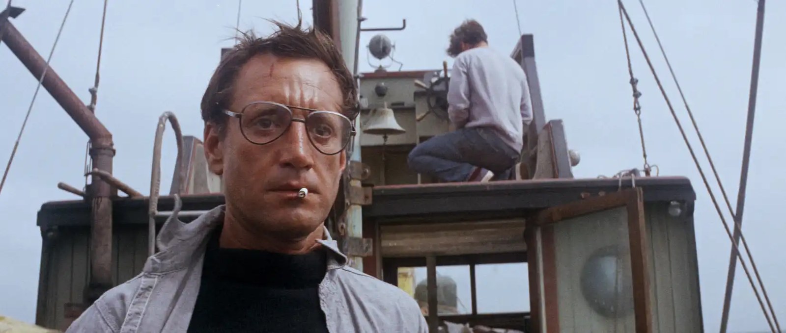 Roy Scheider as Hooper wearing big glasses and smoking a cigarette, stares in shock at the backend of a boat in Jaws